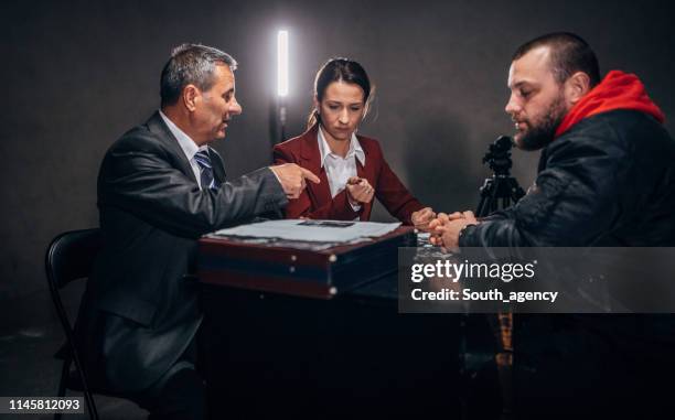 detectives and male prisoner sitting in interrogation room - prosecuting attorney stock pictures, royalty-free photos & images