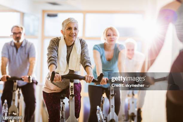 group of athletic mature people having exercising class with an instructor in a gym. - spin class stock pictures, royalty-free photos & images