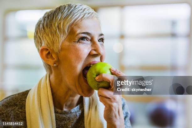 mature athletic woman eating an apple after exercising in health club. - apple bite out stock pictures, royalty-free photos & images