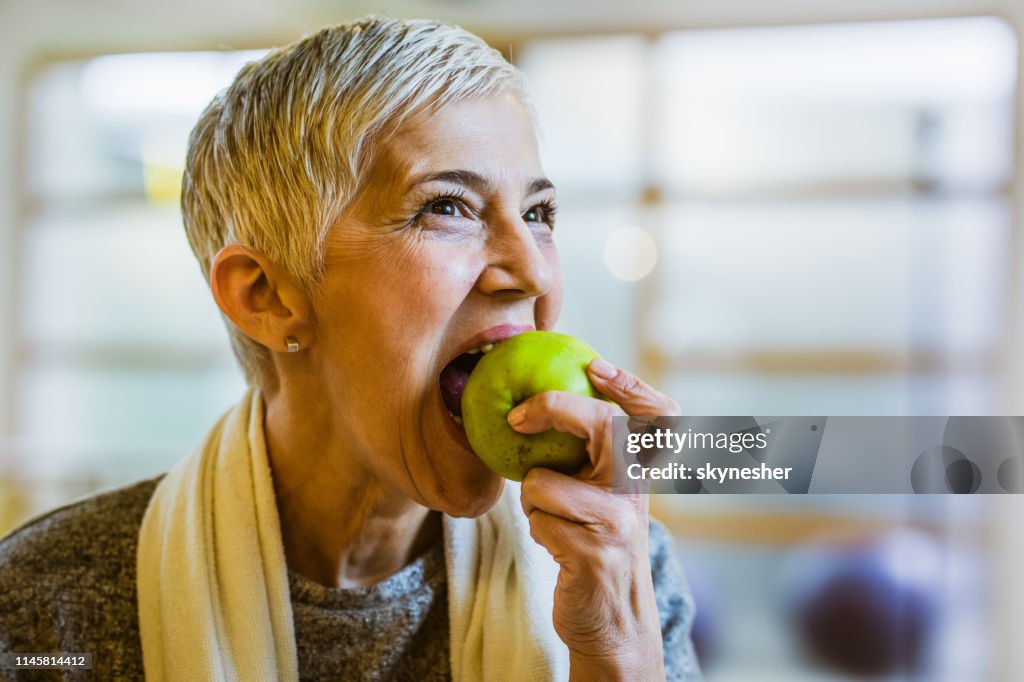 Mulher atlética madura que come uma maçã após o exercício no clube de saúde.