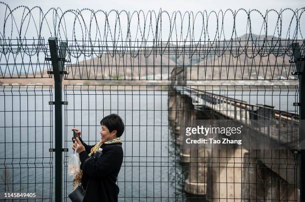 Woman takes photos in front of a fence with razor wire is protecting the border on the Yalu river north of the border city of Dandong, Liaoning...