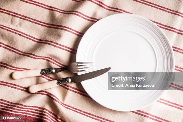 empty white plate, fork and knife on a red and white linen striped napkin, top view. image with copy space. kitchen table with a towel and a plate - top view with copy space. - fasting activity foto e immagini stock