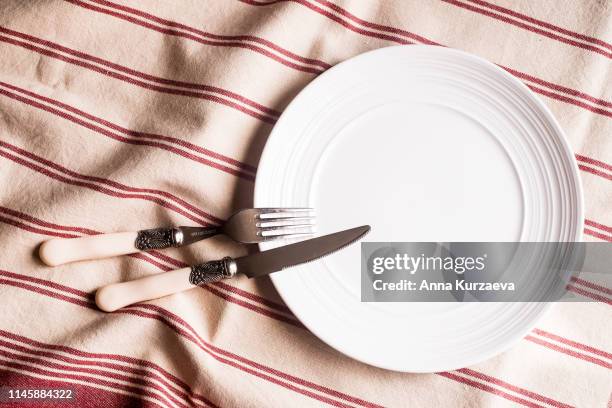 empty white plate, fork and knife on a red and white linen striped napkin, top view. image with copy space. kitchen table with a towel and a plate - top view with copy space. - silverware stock pictures, royalty-free photos & images