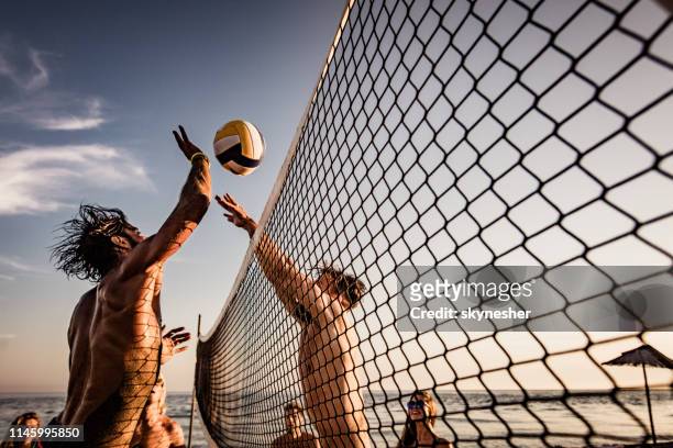 jonge man het blokkeren van zijn vriend tijdens het spelen beachvolleybal in de zomer dag. - volleybal stockfoto's en -beelden