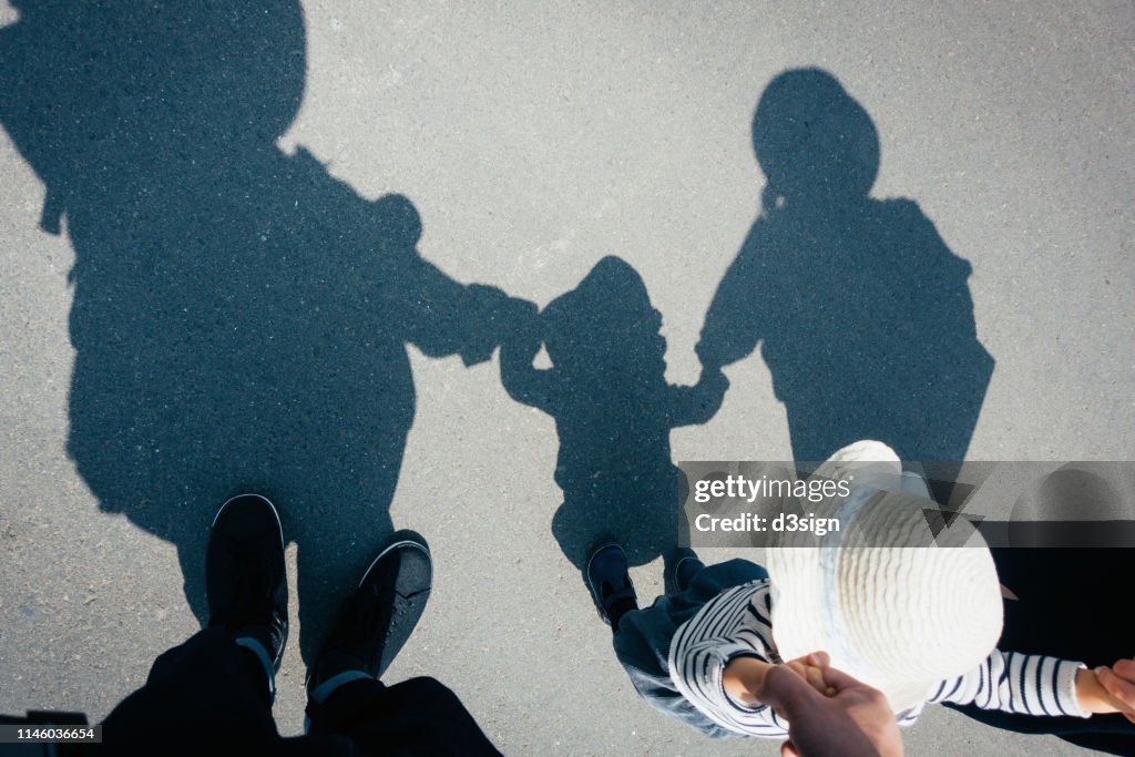 Shadow on gravel path of a loving family of three holding hands walking outdoors on a lovely sunny day