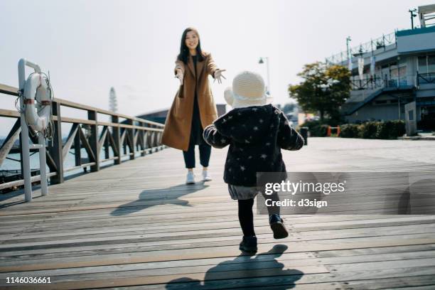 cute little daughter running towards mother on the wooden bridge by the pier on a lovely sunny day - lakeshore park stock pictures, royalty-free photos & images