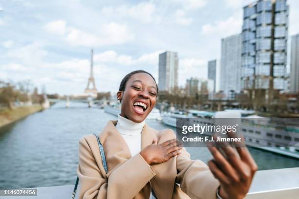 woman taking a selfie with smartphone with the eiffel tower in the background - paris millenials stock-fotos und bilder