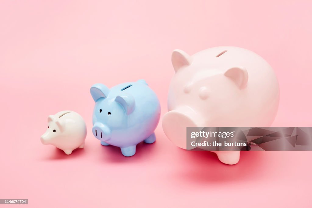 Still life of differently sized white, blue and pink piggy banks in ascending size order on pink background