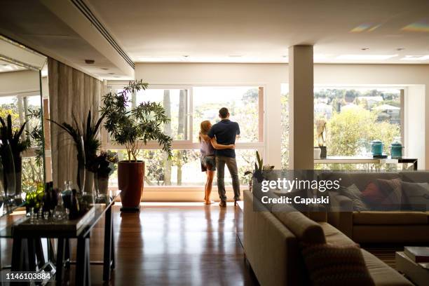 paar bewonderen het uitzicht vanuit de woonkamer van hun huis. - living room window stockfoto's en -beelden