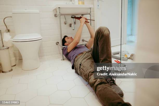 uomo che risolve problemi idraulici nel suo bagno - under sink foto e immagini stock