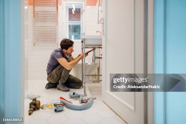 giovane che ripara una perdita sotto il lavandino del bagno - under sink foto e immagini stock