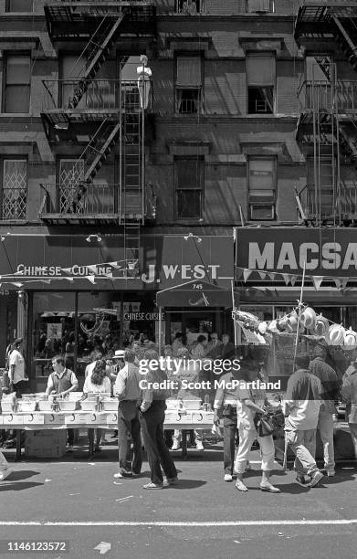 Woman stands on a fire escape and looks down over the pedestrians and vendors on the street in Hell's Kitchen during the International Food Festival,...