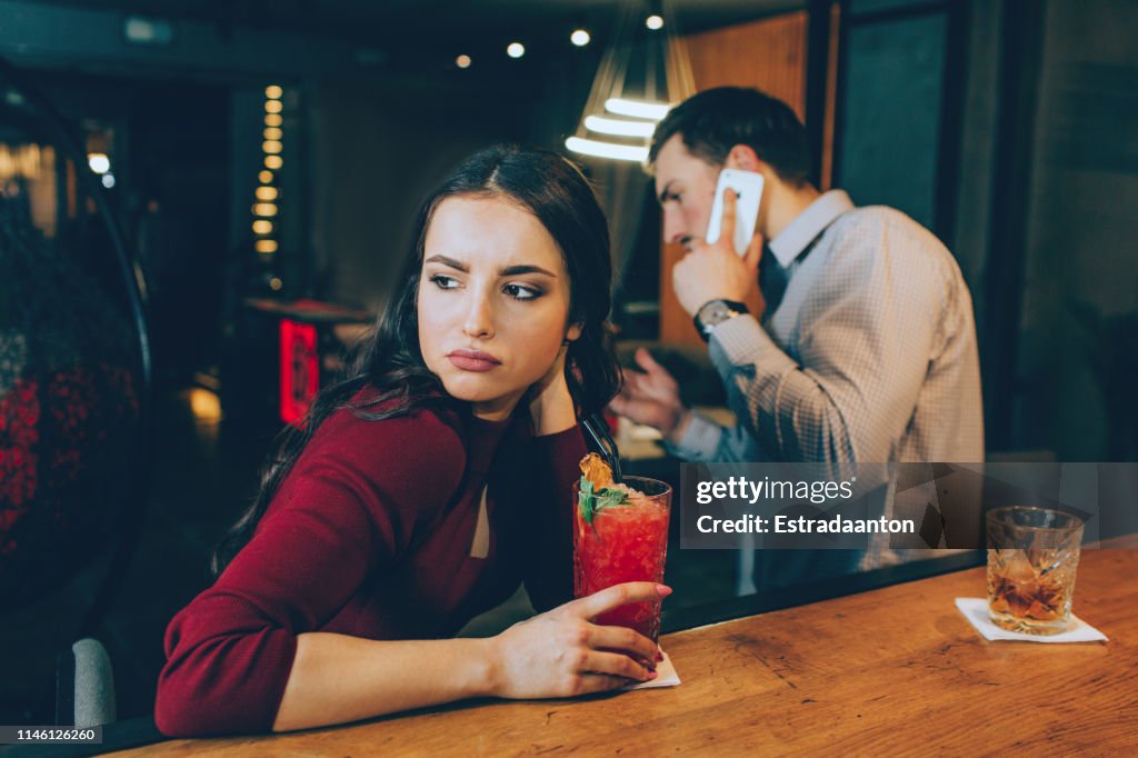 Sad picture of girl looking to the right. She is sad because man is answering to the phone call and not spending time with her. She doesn't have a good mood.