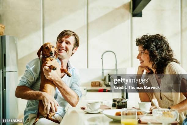 smiling husband holding dog while eating breakfast with family - real wife sharing 個照片及圖片檔