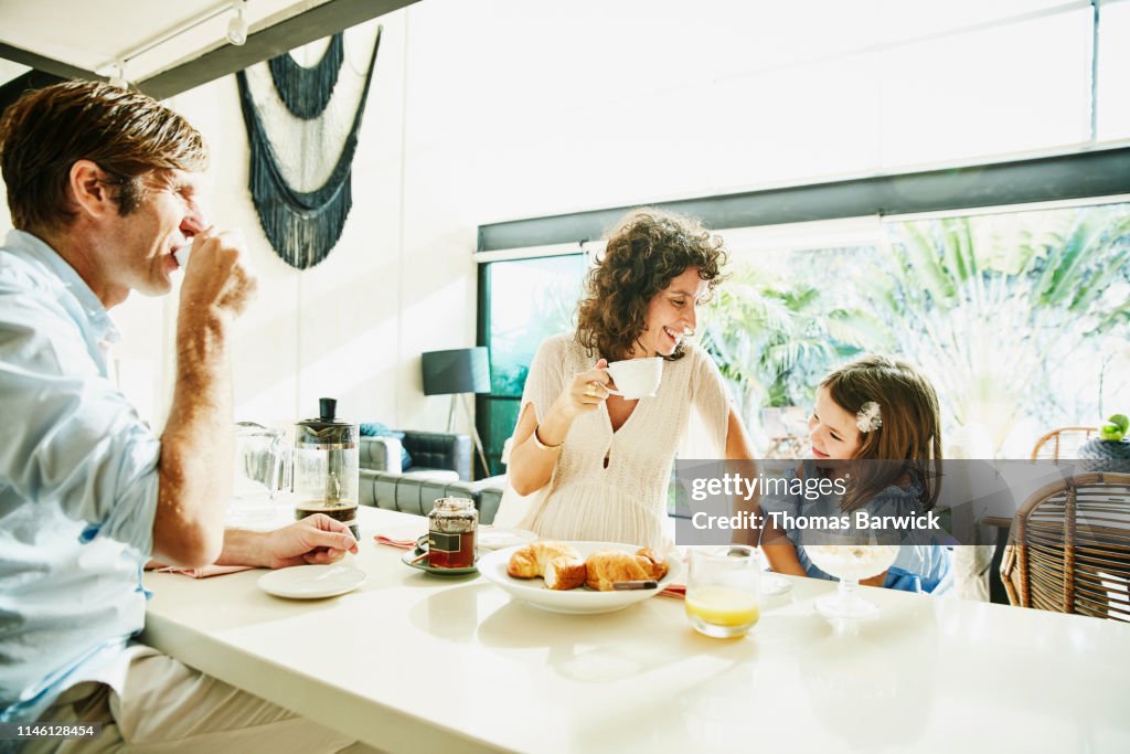 Laughing pregnant mother sharing breakfast at kitchen counter with daughter and husband