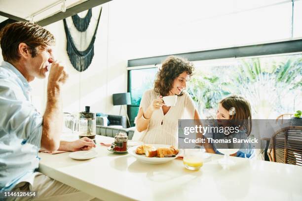 laughing pregnant mother sharing breakfast at kitchen counter with daughter and husband - mum dad daughter stock pictures, royalty-free photos & images