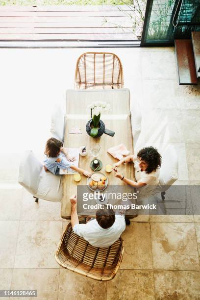 overhead view of smiling wife and husband sharing breakfast with daughter at dining room table - nosotroscollection stockfoto's en -beelden
