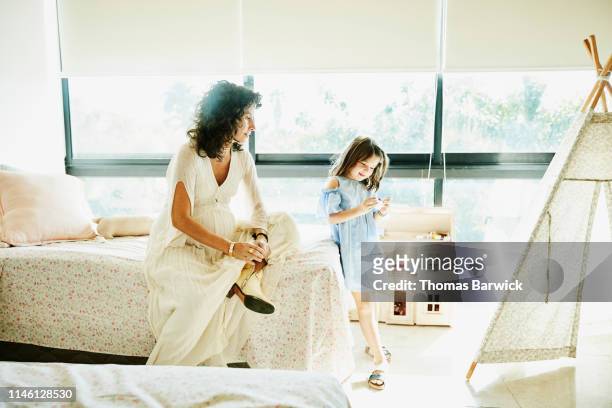 Pregnant mother watching young daughter admire toy in bedroom