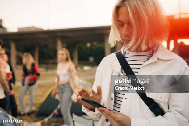 young man using mobile phone at musical event during summer - coat music festival stock pictures, royalty-free photos & images