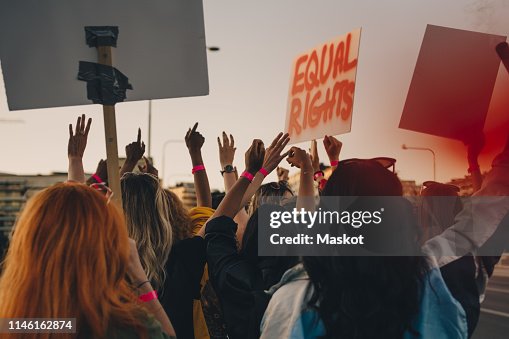 Rear view of young women protesting for equal rights while marching in city Rear view of young women protesting for equal rights while marching in city