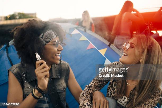 smiling man with eletronic ciagrette looking at woman against tent - electronic cigarette ストックフォトと画像