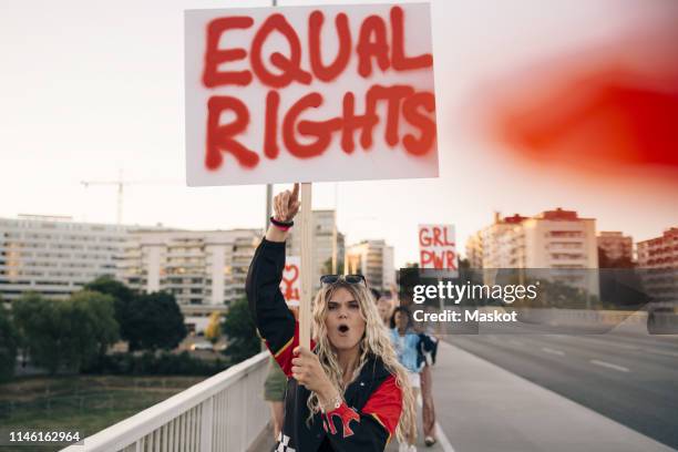 women with poster shouting while marching for equal rights on bridge in city - droits de la femme photos et images de collection