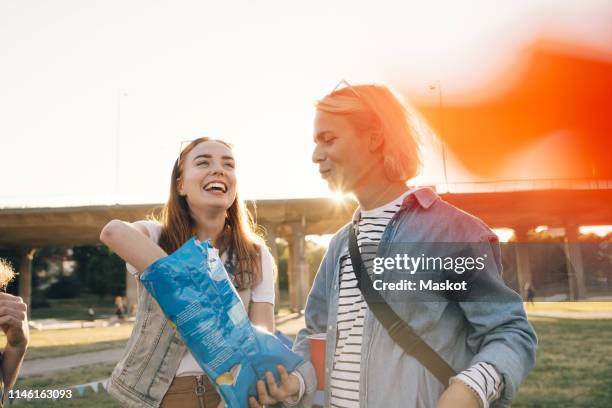 man giving chips packet to happy woman at musical event - snacks stock-fotos und bilder