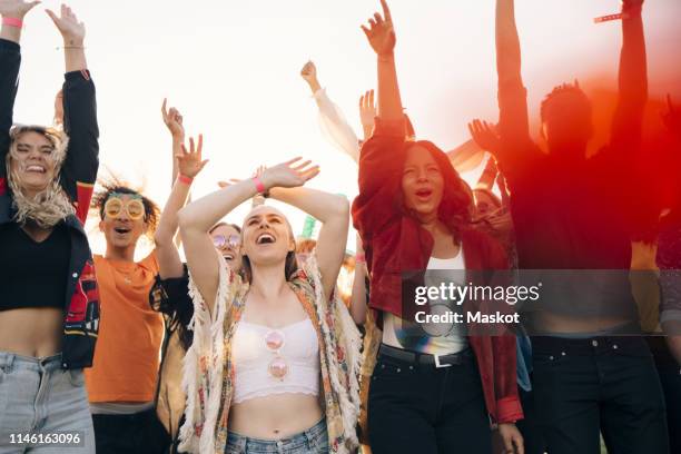 cheerful fans shouting with arms raised against sky during summer - the future of everything festival stock pictures, royalty-free photos & images