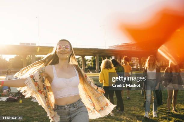 smiling woman dancing with friends in background at event on sunny day - sunny days foto e immagini stock