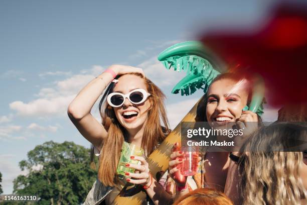 cheerful female friends enjoying drinks at music concert against sky in summer - music festival day 3 foto e immagini stock