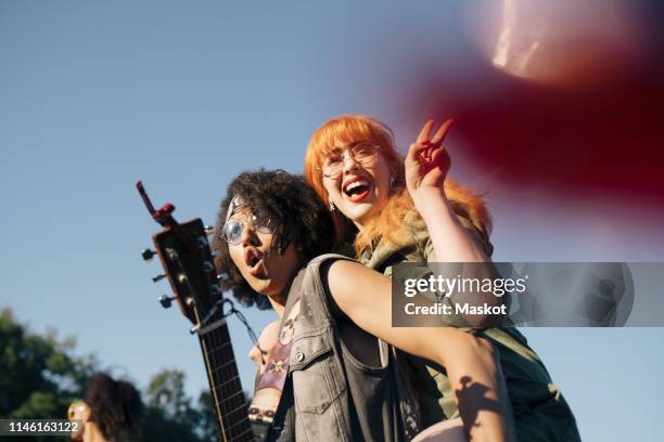 excited man with ukulele piggybacking happy friend in event against sky - youth culture music stock pictures, royalty-free photos & images