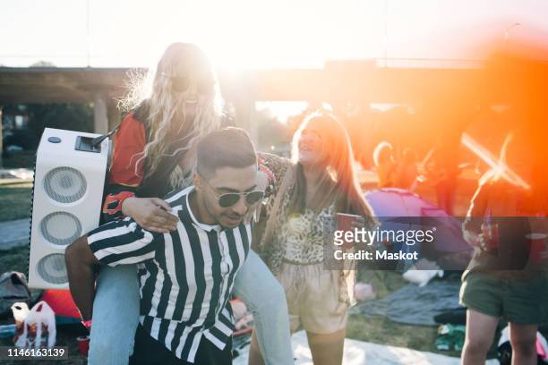 man piggybacking female friend with speaker while enjoying in music festival - tag stock-fotos und bilder