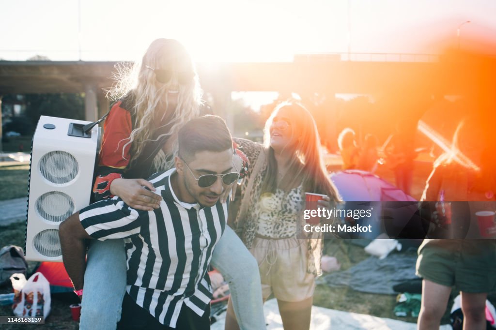 Man piggybacking female friend with speaker while enjoying in music festival