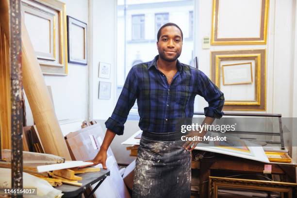 portrait of smiling young male artist standing with hand on hip at framing workshop - large group of craftsman stock-fotos und bilder