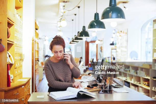 young female sales clerk talking on mobile phone while looking at file in home improvement store - assistant imagens e fotografias de stock