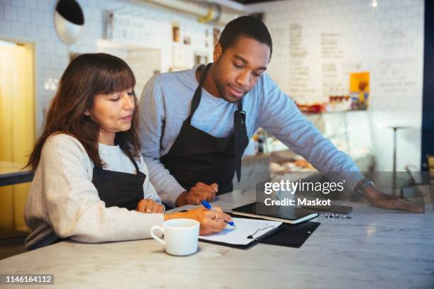 female employee discussing over clipboard with male coworker at table in cafe - order pad stock pictures, royalty-free photos & images