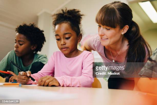 smiling female teacher looking at students drawing in class - schulbeginn stock-fotos und bilder