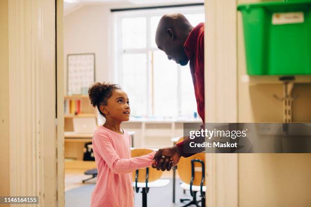 teacher shaking hand with girl at doorway in classroom - students shaking hands stock-fotos und bilder