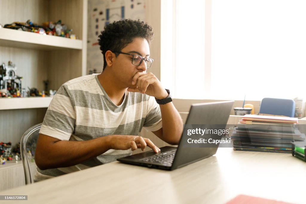 Teenage boy studying with laptop at home
