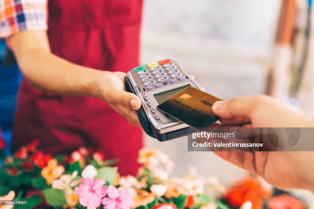 Greenhausarbeiter verkaufen Topfblumen. Kontaktloses Bezahlen mit Kreditkarte