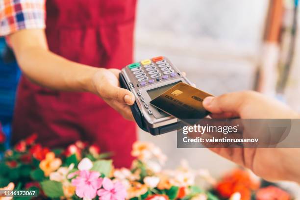 broeikas werkers verkopen van potten bloemen. contactloze betaling met creditcard - cards stockfoto's en -beelden