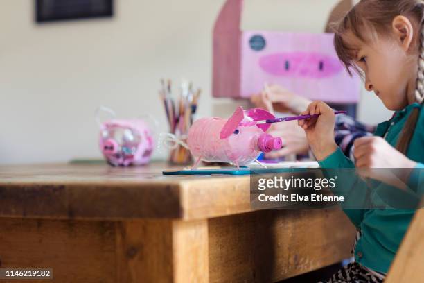 Child (6-7) painting recycled plastic bottle to make a piggy bank