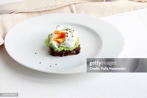 sandwich from poached egg, dark bread, avocado in a white plate on a white background - avocado toast white background stockfoto's en -beelden