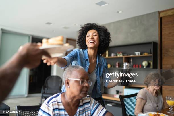 smiling woman holding a bottle of juice and giving a plate of sandwich - sandwich generation stock pictures, royalty-free photos & images