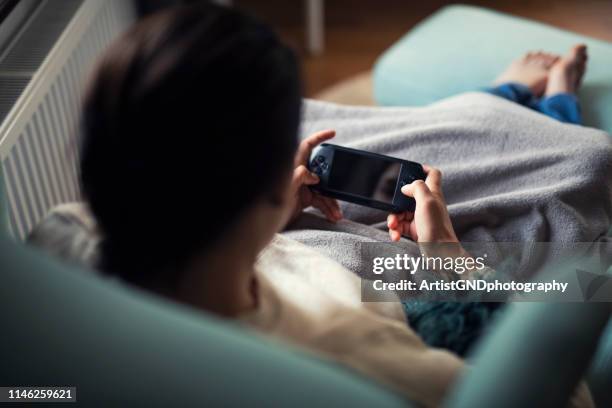 young woman playing portable game at home. - handheld video game stock pictures, royalty-free photos & images