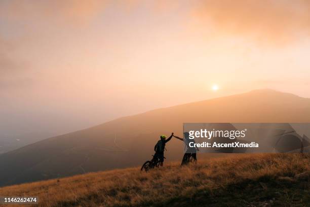 mountain bikers geven high-five bij zonsondergang - forward athlete stockfoto's en -beelden