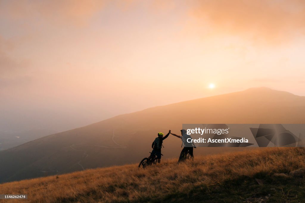 Os motociclistas da montanha dão elevado-cinco no por do sol