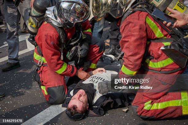 French firemen help an injured Gilet Jaune or 'Yellow Vest' protestor hit by a police grenade as demonstrations for International Labour Day turn...