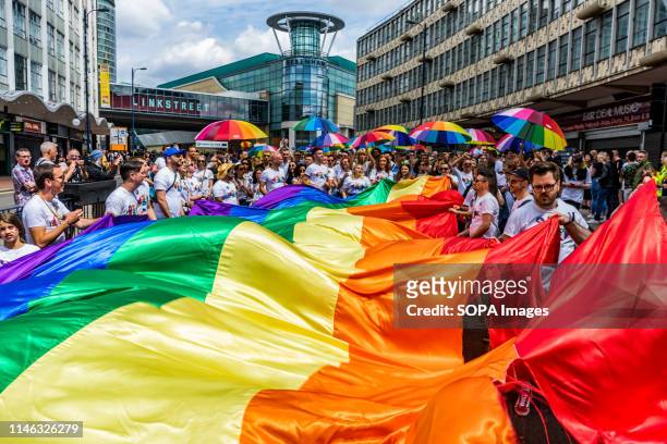 Members of the LGBTQ community are seen holding a rainbow flag and umbrellas during the Birmingham Pride parade. Birmingham Pride this year is...
