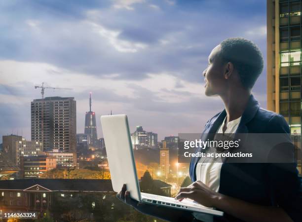 businesswoman holding laptop by city skyline at sunset in nairobi, kenya - nairobi - fotografias e filmes do acervo